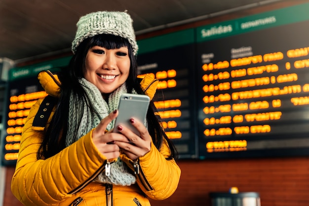 Donna asiatica turistica che utilizza cellulare nella stazione ferroviaria. Concetto di turismo.