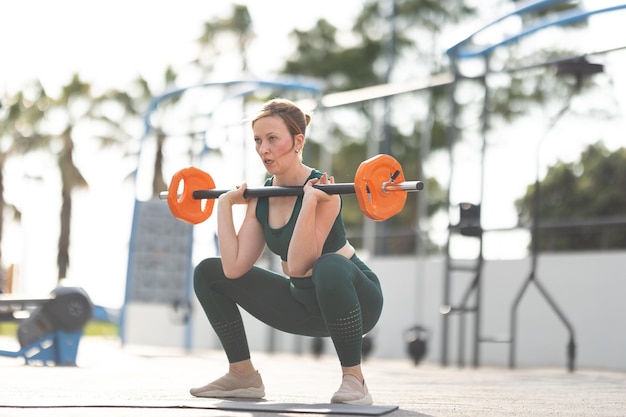 Donna atletica adulta accovacciata con manubri nelle sue mani in piedi sul campo sportivo