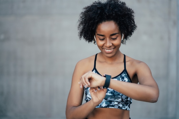 Donna atletica afro che controlla il tempo sul suo orologio intelligente mentre si allena all'aperto