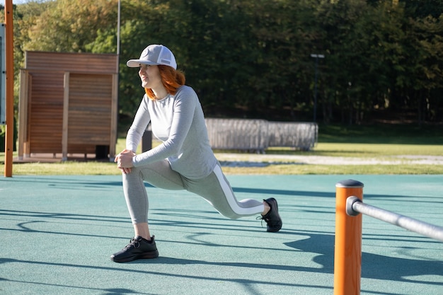 Donna atletica allo zenzero che si scalda per l'allenamento mattutino all'aperto sul campo sportivo urbano in autunno soleggiato...