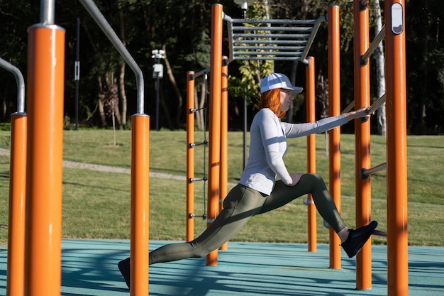 Donna atletica allo zenzero che si scalda per l'allenamento mattutino all'aperto sul campo sportivo urbano in una giornata di sole autunnale.