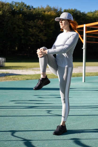 Donna atletica allo zenzero che si scalda per l'allenamento mattutino all'aperto sul campo sportivo urbano in una giornata di sole autunnale.