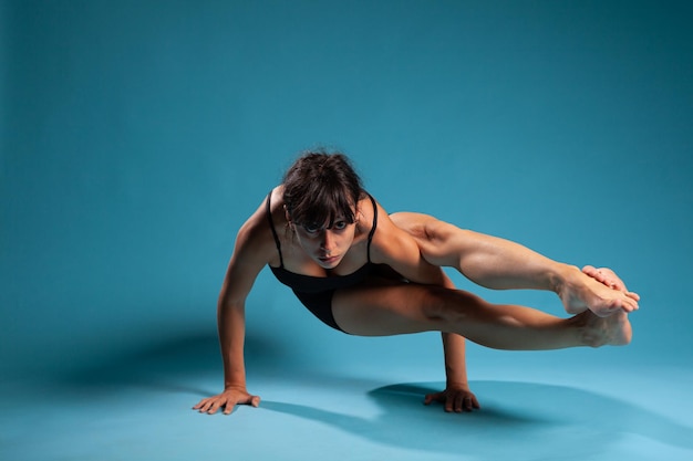 Donna atletica attiva in piedi nelle mani che lavorano al bilanciamento del braccio in studio con sfondo blu. Personal trainer che pratica esercizi in palestra che allungano i muscoli del corpo durante l'allenamento sportivo