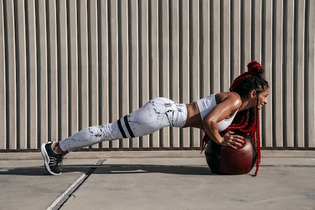 Donna atletica che fa esercizi di flessioni con palla medica Forza e motivazioneFoto di donna sportiva in abbigliamento sportivo alla moda