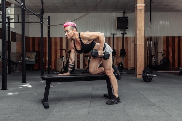 Donna atletica che fa esercizio di fila con manubri con una mano. Allenamento muscolare della schiena. Bodybuilding e Fitness