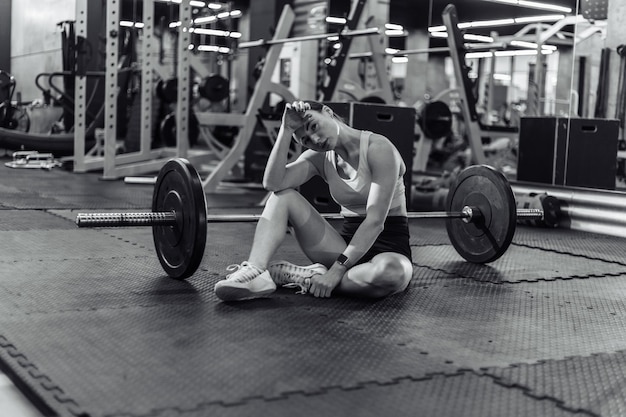 Donna atletica che riposa dopo un allenamento intenso e intenso con il bilanciere in palestra