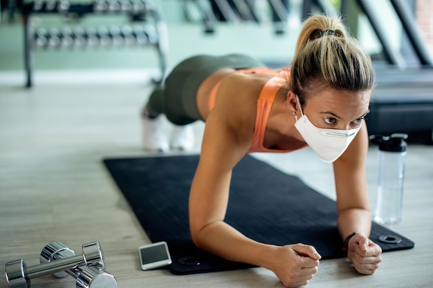 Donna atletica con maschera facciale che si esercita nella posa della tavola in palestra