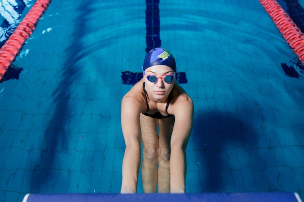 Donna atletica in cappello e occhiali da nuoto pronti per iniziare la gara di nuoto in piscina