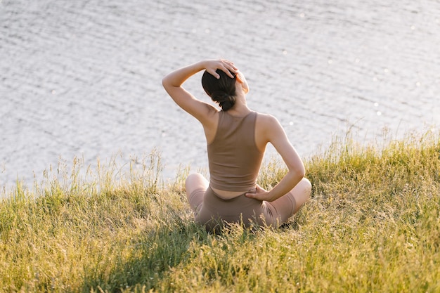 Donna atletica seduta nella posizione del loto e praticare yoga all'aperto al tramonto vista posteriore