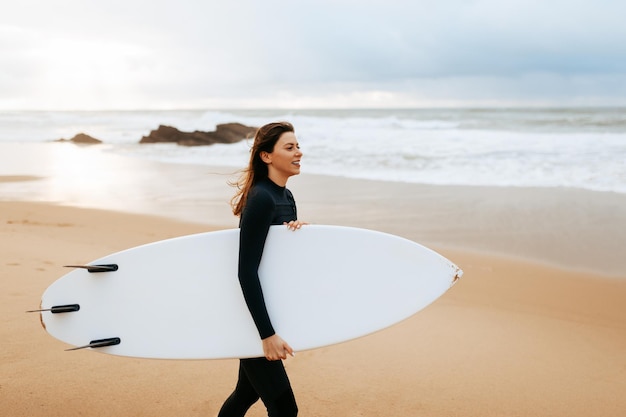 Donna attiva che cammina con la tavola da surf in acqua con un'espressione felice vestita con abiti speciali