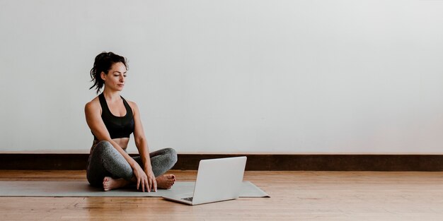 Donna attiva che impara lo yoga online tramite un laptop