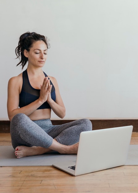 Donna attiva che impara lo yoga online tramite un laptop