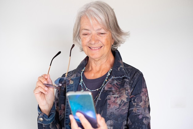 Donna attraente anziana che tiene gli occhiali utilizzando lo smartphone per la comunicazione online tramite video