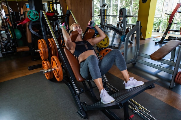 Donna attraente caucasica che pratica squat nella macchina ginnica in palestra