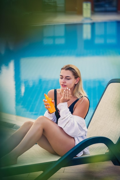 Donna attraente che applica la protezione solare sul viso in piscina Fattore di protezione solare per le vacanze