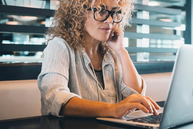 Donna attraente che lavora al computer portatile alla scrivania in un luogo di coworking o in un ufficio moderno Moderna donna d'affari alla moda che utilizza il computer da sola per un lavoro online Freelance professionista al lavoro con la tecnologia