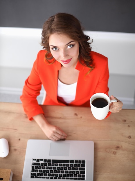 Donna attraente che si siede alla scrivania in ufficio che lavora con il computer portatile