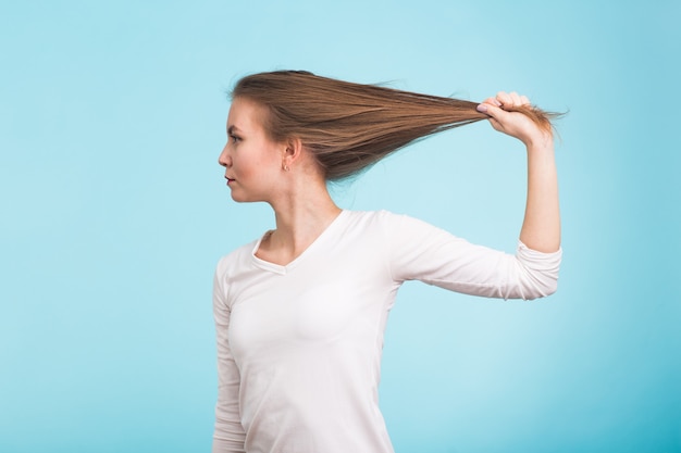 Donna attraente che tiene ai capelli. Capelli sani e forti su sfondo blu.