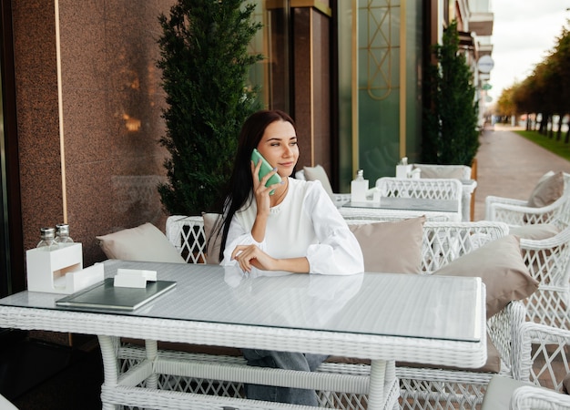 Donna attraente con un sorriso carino che parla al cellulare mentre si rilassa in un caffè.