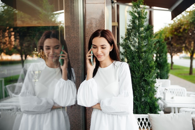 Donna attraente con un sorriso carino che parla al cellulare mentre si rilassa in un caffè.