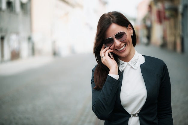 Donna attraente di affari che cammina e che parla sul telefono cellulare in una via della città.