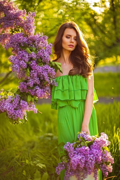 donna attraente in abito verde in posa vicino a decorazioni floreali lilla.