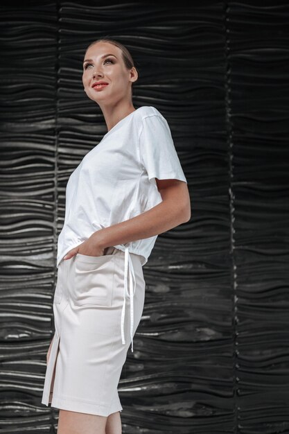 Donna attraente in maglietta bianca e gonna in mezzo a un muro nero elegante dell'ufficio