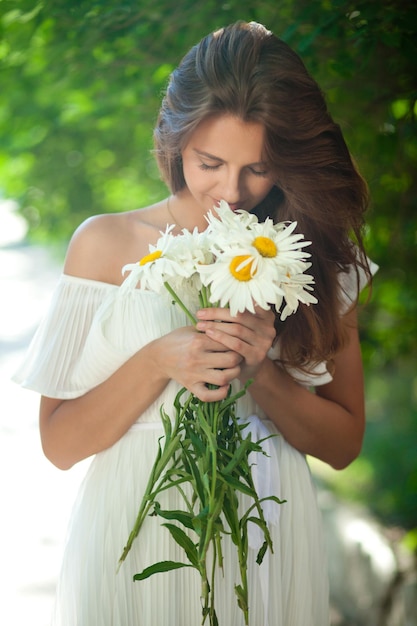 Donna attraente in un vestito estivo bianco che tiene un mazzo di margherite