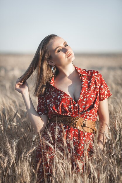 Donna attraente in un vestito rosso sul campo di grano