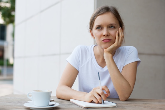 Donna attraente pensosa che lavora al caffè all&#39;aperto