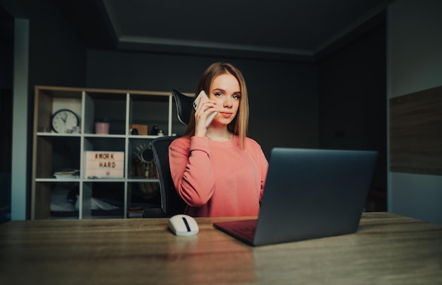 Donna attraente seduta a casa a un tavolo con un laptop e lavorando in remoto guardando la telecamera