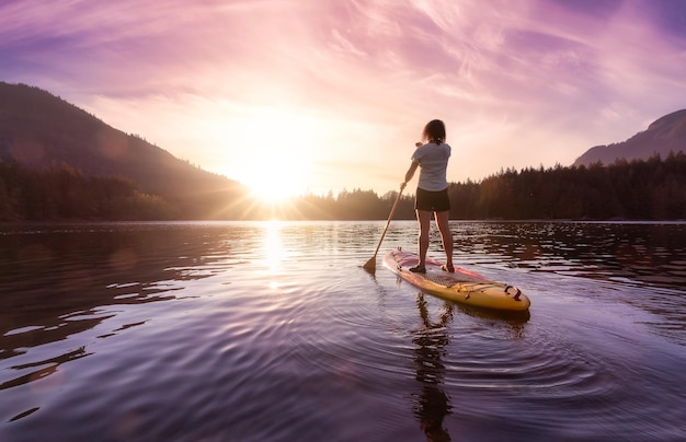 Donna avventurosa che rema su un paddle board in un lago tranquillo