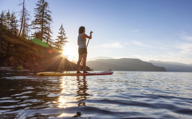 Donna avventurosa che rema su un paddle board in un lago tranquillo