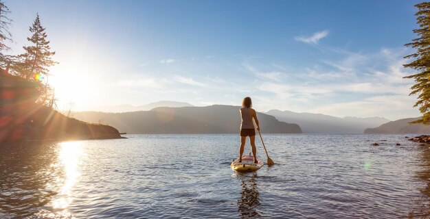 Donna avventurosa che rema su un paddle board in un lago tranquillo