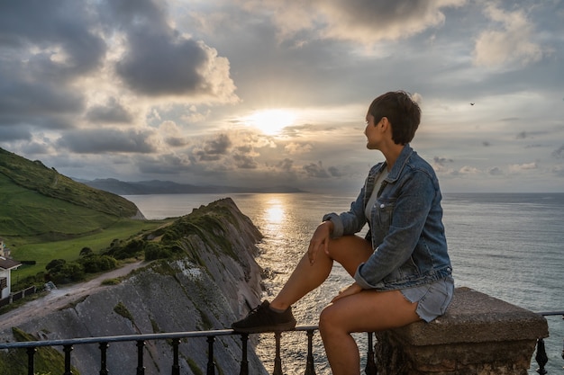 Donna avventurosa del viaggiatore che fa un giro turistico nella destinazione di viaggio delle scogliere di Zumaia. Vista panoramica orizzontale della donna che viaggia nel paese vasco. Persone e viaggi nel concetto di Spagna.