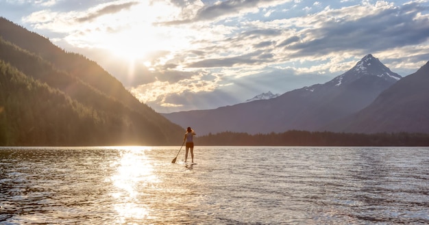 Donna avventurosa paddle boarding in un lago intorno al paesaggio montano canadese