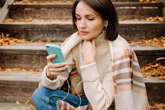 Donna avvolta in una coperta e utilizza lo smartphone