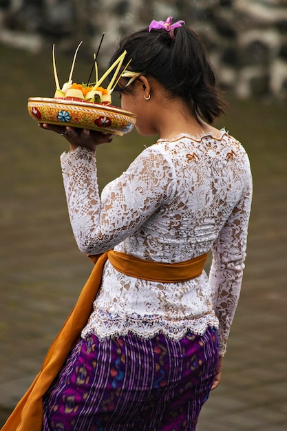 Donna balinese vestita tradizionalmente portando offerte al tempio per i rituali mattutini, Ubud, Bal