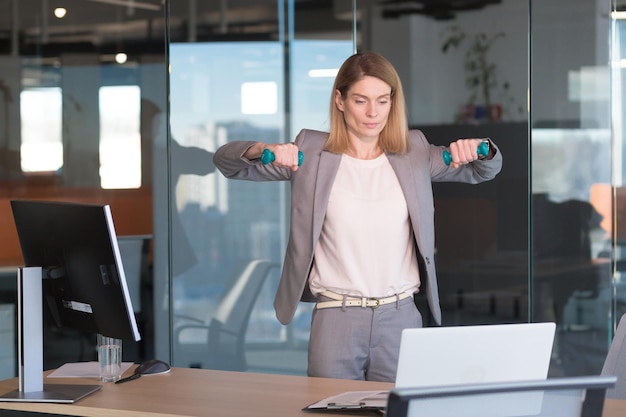 Donna bella e felice che fa esercizi sportivi in ufficio al lavoro durante una pausa donna d'affari controlla la salute impegnata nel fitness