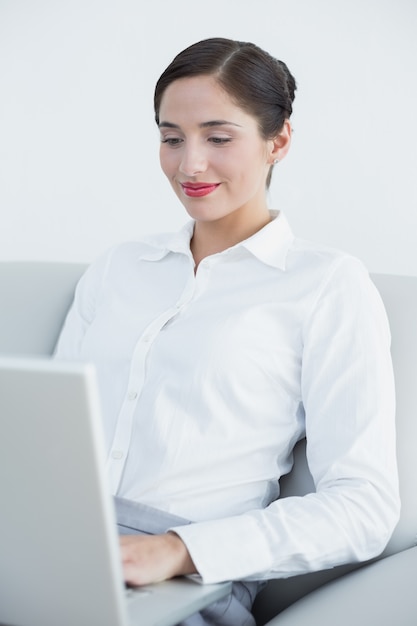 Donna ben vestito sorridente che per mezzo del computer portatile sul sofà