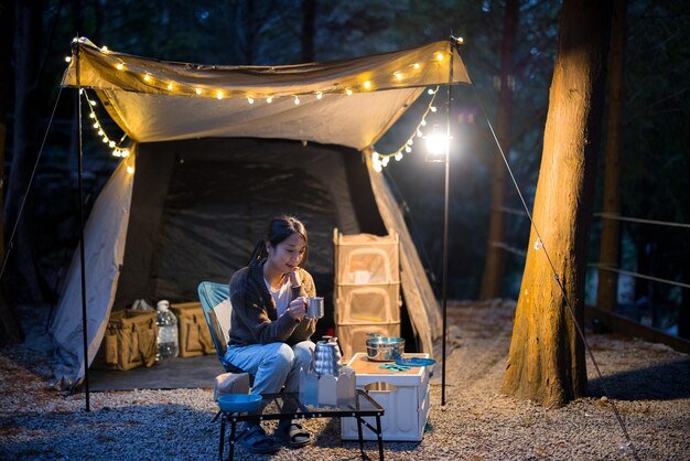 Donna beve caffè caldo e si siede all'interno del rifugio della tenda da campeggio la sera