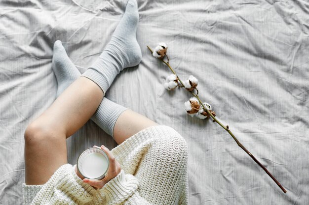 Donna bianca che si siede sul letto con latte caldo in inverno