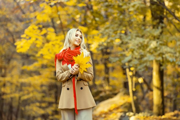 Donna bionda affascinante attraente che cammina nella foresta autunnale bella donna che indossa cappotto caldo e re