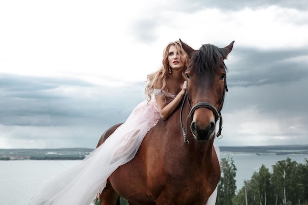 Donna bionda alla moda che monta un cavallo in una giornata nuvolosa Capelli ricci lunghi