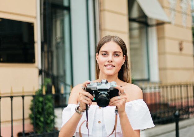 Donna bionda allegra che tiene retro macchina fotografica nell'ambiente urbano