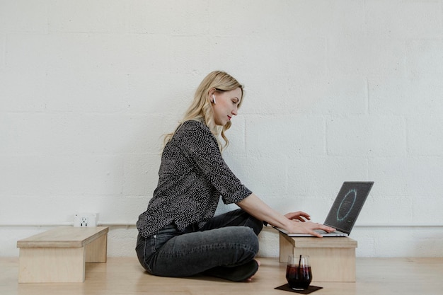 Donna bionda allegra che utilizza un computer portatile su un pavimento di legno