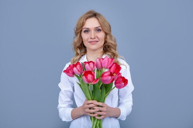 Donna bionda allegra con fiori di tulipano di primavera su sfondo grigio