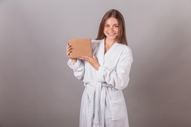 Donna bionda brasiliana che mostra capelli meravigliosi vestiti con una veste che tiene piccole scatole di cartone con cosmetici