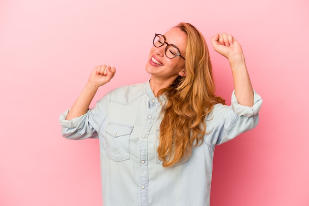 Donna bionda caucasica isolata su sfondo rosa che celebra un giorno speciale, salta e alza le braccia con energia.