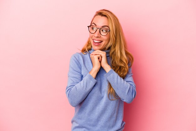 Donna bionda caucasica isolata su sfondo rosa pregando per la fortuna, stupita e aprendo la bocca guardando in avanti.